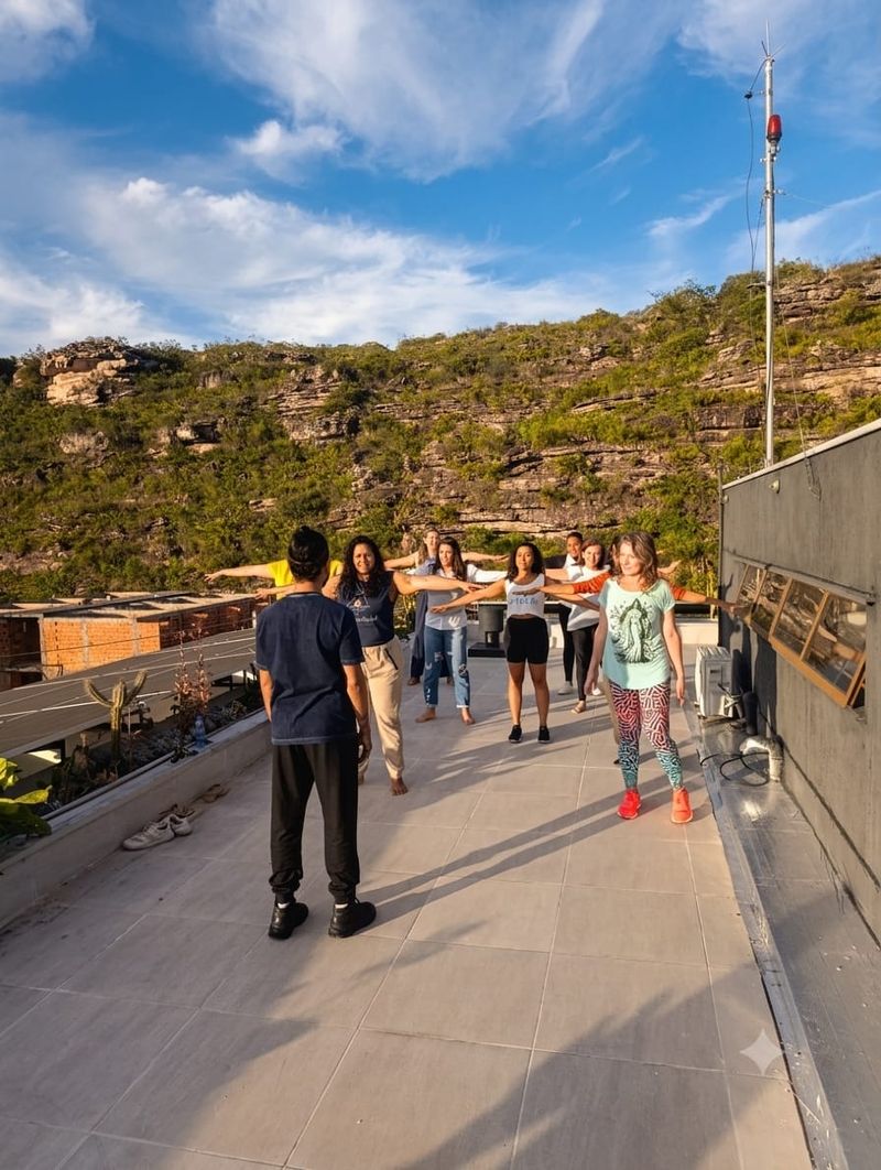Grupo em círculo, com os braços abertos, durante a vivência de dançaterapia em um terraço