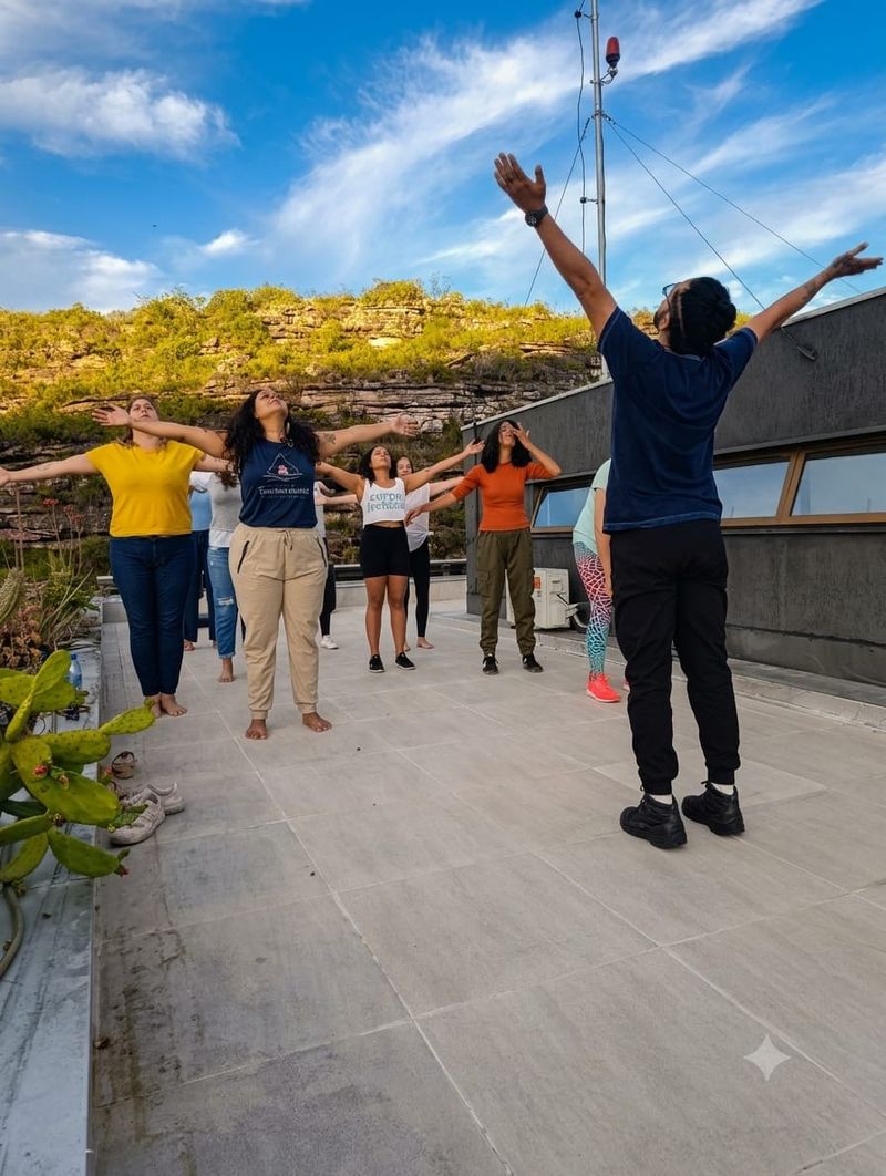 Grupo com os braços elevados durante a vivência, sob o céu azul